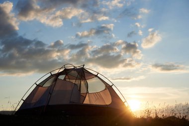Çadırın altında nadir bulutlar ve bulanık bir arka plan üzerinde akşam güneşi ile gökyüzü gün batımında bir dağın tepesinde duruyor. Dağlarda sağlıklı rekreasyon kavramı