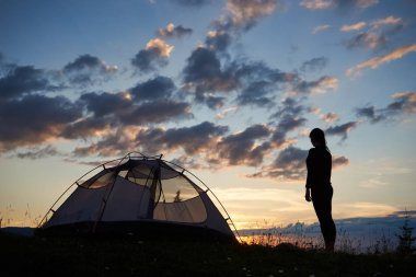 Daybreak zevk güzel sahne günbatımı nadir bulutlarda akşam gökyüzünde, kır çiçekleri bir çim üzerinde kamp yakınındaki dağın tepesinde duran kız backpacker silüeti arkadan görünüm.