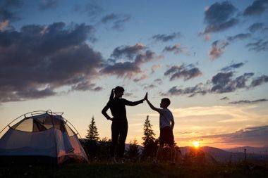Genç bir kadın ve diğer her bir dağın zirvesinde şafak bir kamp yakınındaki bir beşlik veren bir çocuk silüeti. Köknar-ağaçlar ve dağlar ve tepeler üzerinde yükselen güneş güzel bir manzara