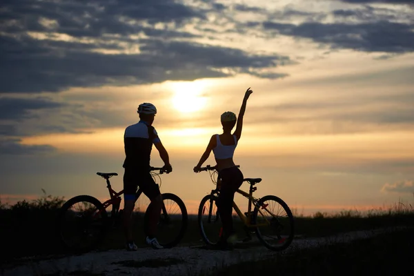 后视图的一对夫妇骑自行车站在享受日落 男子和妇女身着头盔和运动服 — 图库照片