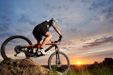 Yalnız ve haddeleme tepeden aşağı bisiklet sürme spor giyim ve kask, aktif erkek bisikletçi. Sportif ve sağlam adam güzel gün batımı ve akşam arka plan gül-mavi gökyüzüne karşı Bisiklete binme