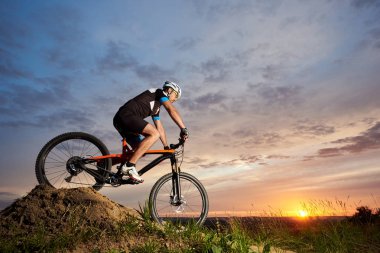 Enerjik ve aktif adam kask ve spor giyim akşamları turuncu bisiklet sürme görünümünü. Oturma ve günbatımında tepeden aşağı yuvarlanan sportif ve enerjik atlet. Recreative temiz hava faaliyetleri.
