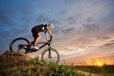 Yalnız ve haddeleme tepeden aşağı bisiklet sürme etkin bisikletçi spor giyim ve kask giyiyor. Güzel gün batımı ve gül-mavi gökyüzü arka plan karşı Bisiklet sportif ve sağlam adam.