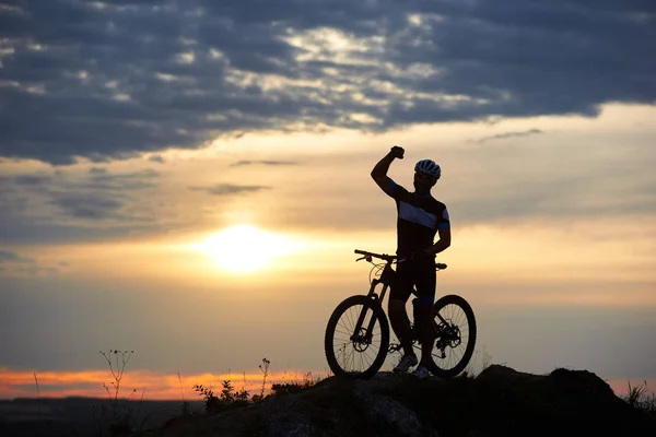运动的微笑的人站在岩石上的石头上 在一个美丽的夕阳的模糊背景的山上 这个男人穿着运动服和头盔 — 图库照片