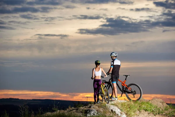 夫妇站在他们的山地自行车附近的岩石山和观察美丽的景观 日落和多云的天空 — 图库照片
