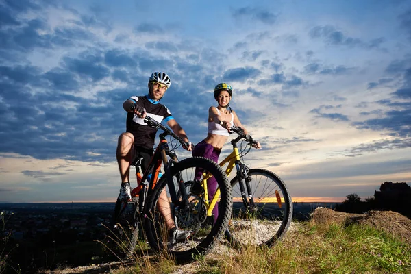 Gençler üzerinde günbatımında sihirli bir gökyüzünün altında bir tepenin üstüne dağ bisikleti. 