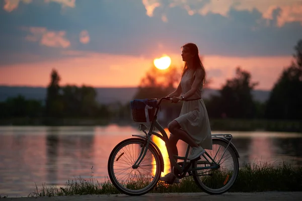 자전거를 로맨틱 소녀가 페달을 호수에서 보라색 석양을 바라보고 있습니다 — 스톡 사진