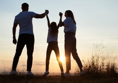 Anne ve kızının silueti şehir dışında eğlenceli bir gün geçiriyorlar akşamları, baba ve anne kızın elini tutuyorlar ve o asılıyor, geriye bakıyor.