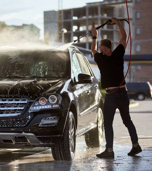 Bonito Homem Segurando Uma Mangueira Lavar Seu Carro Preto Com — Fotografia de Stock