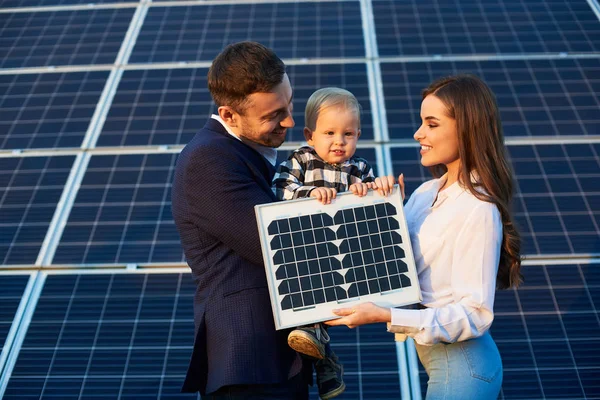 Young happy family on the background of solar panels. A man, woman and child are holding a solar panel in their hands and smiling. Solar energy, modern technologies concept image