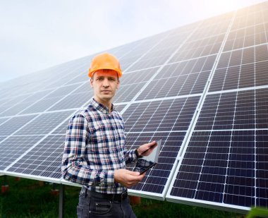 Güneş panelleri istasyonunun yanında elinde tabletle duran miğferli bir insan mühendisi portresi. Yeşil ekolojik enerji üretimi. Ev yapımı.