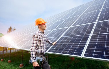 Elinde tablet olan kasklı genç adam güneş panellerinin yanında duruyor. Yeşil ekolojik enerji üretimi. Güneş istasyonu geliştirme konsepti. Ev yapımı.