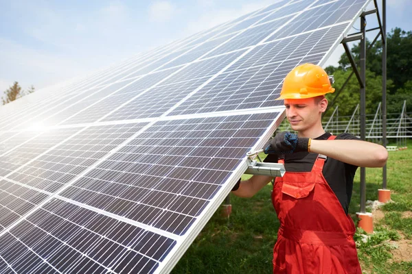 Male technician checks the maintenance of the solar panels. Orange safety cap on his head. Concept: renewable energy, technology, electricity, service, green power.
