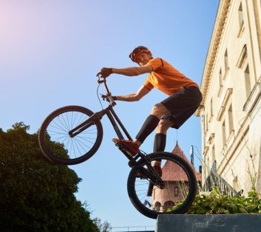 Low angle view of a trial biker standing on a back wheel of mountain bike keeping balance looking at camera, concept of active lifestyle