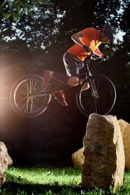 Side view of strong man in sportswear holding a black bicycle. Athlete in helmet training in evening on a bicycle. Concept of training.