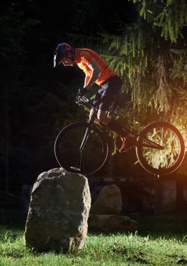 Akşamları büyük kayalıklarda, parkta, yan manzarada, etkin yaşam tarzı kavramında ön tekerde performans sergileyen yetenekli motosikletçilerin olağanüstü gösterisi.