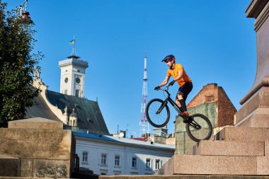Horizontal side view of a freestyle trial biker performing extreme show on monument pedestal downtown, concept of active lifestyle, copy space
