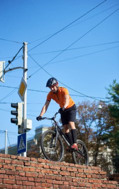 Young sportsman standing on a brick wall with his mountain bike. Blue sky with power lines on background