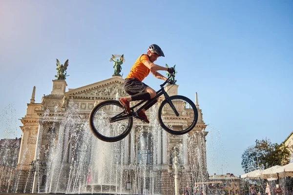 Вид Снизу Активного Парня Оранжевой Рубашке Черным Велосипедом Архитектурном Фоне — стоковое фото