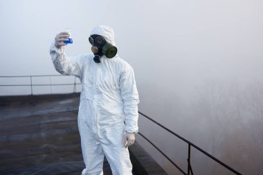 Erkek araştırmacı, yüksek katlı bir binanın tepesinde duruyor. Örnekler üzerinde araştırma yapıyor. Kirlenmiş bölgede toplanıyor.