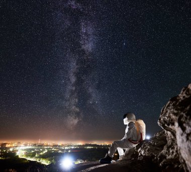 Bir yandan uzay yolcusu kayalık dağda oturuyor ve güzel yıldızlı gökyüzünün, Samanyolu 'nun, vadideki gece şehrinin tadını çıkarıyor. Yıldızlar arasında kozmonot kavramı, uzay yolculuğu