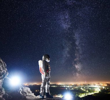 Görev uzmanı uzay adamı kayalık tepede duruyor ve Samanyolu ile güzel yıldızlı gökyüzüne bakıyor. Uzay yolcusu beyaz uzay giysisi ve miğfer giyiyor. İnsan uzay keşfi kavramı.