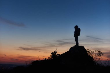 Kayalık tepenin üstünde duran astronot silueti ve arka planda güzel bir gece gökyüzü. Uzay yolcusu kasklı uzay elbisesi giyiyor. Uzay yolculuğu kavramı.