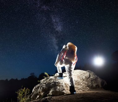 Uzay yolcusunun yıldızlı güzel gece gökyüzünün altında kayalık kayalıklara tırmanışının arka görüntüsü. Uzay giysili kozmonot yeni gezegeni keşfediyor. Evrende uzay yolculuğu, galaksi ve insan kavramı.