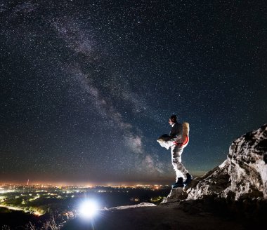 Kozmonot kayalık tepede yıldızlarla ve Samanyolu 'yla gece gökyüzünün altında duruyor. Uzay giysili uzay yolcusu miğfer tutuyor ve gece şehir ışıklarına bakıyor. Kozmonotlar ve gece vakti kavramı