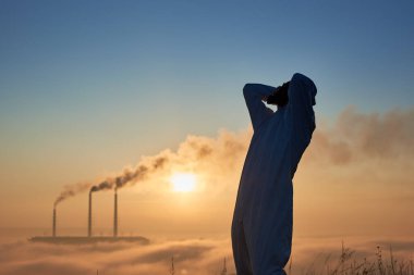 Radyasyon giysisi içindeki çevreciler umutsuzluk içinde başını tutarken bacalar atmosfere zehirli gazlarla dolu yoğun dumanlar üretiyor. Gaz maskeli bilim adamı elleriyle başını tutuyor. Felaket kavramı