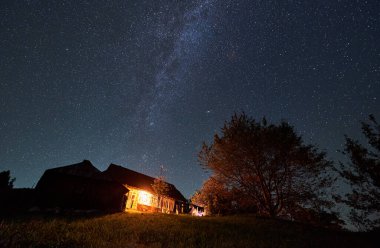 Geceleri ağaçlarla çevrili, dağlardaki bir yazlığın yatay görüntüsü Samanyolu takımyıldızıyla muhteşem bir yıldızlı gece.