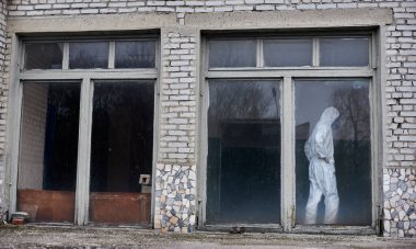 Geniş pencereli eski tuğla evin içinde duran çevreci bir erkek. Elektrik santralindeki çevre sorunlarını araştırırken beyaz koruyucu giysi ve gaz maskesi giyen bilim adamları.