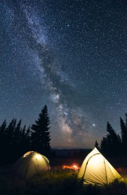 Dağlarda turist kampı, sıcak bir yaz akşamı. İki aydınlık çadır ve kamp ateşi yıldızlarla dolu gece göğü ve parlak Samanyolu 'nun altında yanıyor. Kamp kavramı.
