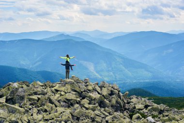 Arka planda poz veren çift, erkeğin omuzlarında oturan kadın, arka planda güzel dağ manzarası. Turistler birlikte zirveye ulaşıyor. İnanılmaz manzaralı vahşi doğa. Spor turizmi.