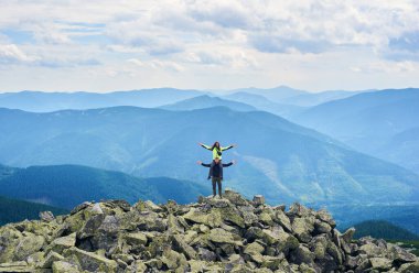 Mutlu çiftin poz verişini, kadının erkeğin omuzlarında oturuşunu, arka planda güzel bir dağ manzarası. Turistler birlikte zirveye ulaşıyor. İnanılmaz manzaralı vahşi doğa. Spor turizmi.