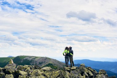 Arkadaki manzara, Karpat Vadisi 'nin güzel dağları ile zirvede taşların üzerinde duran gençler. Rüzgarlı bir günde kız ve erkek bulutlu gökyüzünün altında ceket giyiyor. Etkin yaşam biçimi