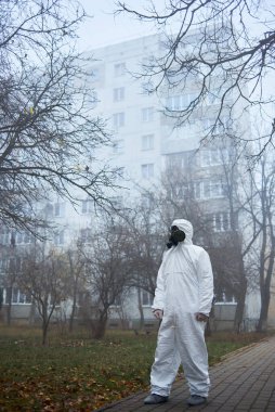 Bilim adamının uzun bir portresi yana bakıyor. Gaz maskeli ve koruyucu kostümlü bir adam ara sokakta poz veriyor.