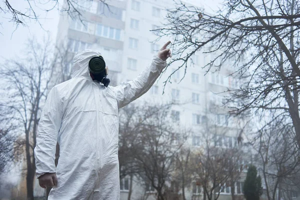 科学家用手指尖着 站在秋天的树间 身穿防毒面具和防护服的男子在空旷的城市靠近建筑物的地方摆姿势 — 图库照片