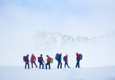 Tepe yamacındaki vadide kar kaplı sırt çantalı yürüyüş ekibi, yürüyüş sırasında dinlenirken kış dağlarının manzarasına hayran kaldılar. Seyahat, yürüyüş ve dağcılık kavramı.