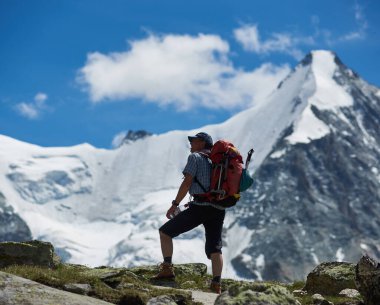 Zinal, İsviçre - 19 Temmuz 2019: Sırt çantalı gezgin elinde su şişesi ve dağlardaki yürüyüş sırasında mavi gökyüzünün altındaki karlı tepelerin keyfini çıkarıyor. Seyahat kavramı, dağcılık..