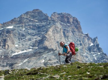 Sırt çantalı gülen gezgin kayalık yamaçlarda yürüyor. Dağlık bölgede tek başına seyahat eden, Matterhorn ya da Monte Cervino 'ya tırmanan bir yürüyüşçü. Yürüyüş, dağcılık kavramı