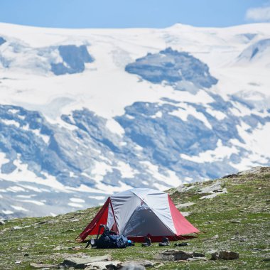 Turist çadırı ve yürüyüş eşyalarıyla dağ vadisinin güzel manzarası. Kamp çadırının görkemli kayalık tepeleri ve arka planda zirvesi olan manzarası. Seyahat kavramı, Alplerde kamp.