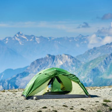 Alplerdeki dağ vadisinde duran yeşil turist çadırı manzarası muhteşem kayalık tepeler, arka planda mavi gökyüzü. Doğa güzelliği kavramı, turizm, seyahat, kamp. Güneşli yaz günü.