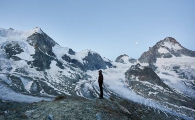 Yanlız turistin güzel dağların manzarasını akşam gökyüzünde ay ışığını seyretmesi. Gezinti, dağ yürüyüşü, zirveye ulaşan adam. İnanılmaz manzaralı vahşi doğa. İsviçre 'de spor turizmi.
