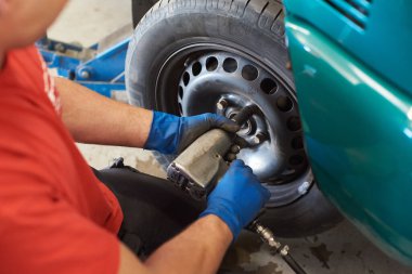 Erkek ellerinin mavi eldivenli, bijon somunları taktığını gördüm. Garajda çalışırken ingiliz anahtarı kullanan profesyonel bir tamirci. Otomatik servis kavramı.