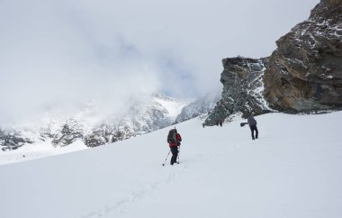 Sırt çantalı turistler kış dağlarında yokuş yukarı yürüyüp dağların zirvesine çıkıyorlar. Seyahat, yürüyüş ve dağcılık kavramı.