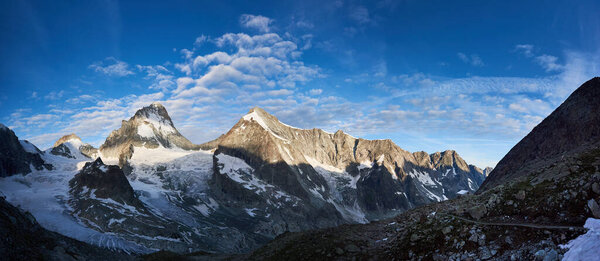 New day in the Swiss Alps, morning bright sun is shining at the ridge of rocky mountains Ober Gabelhorn and Dent Blanche, while the valley is still in the shadow, panoramic shot