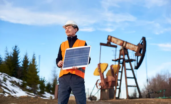 微笑的商人拿着手提式太阳能电池板 男工站在油田的土地上 背景模糊 泵孔模糊 石油工业和替代能源的概念 — 图库照片