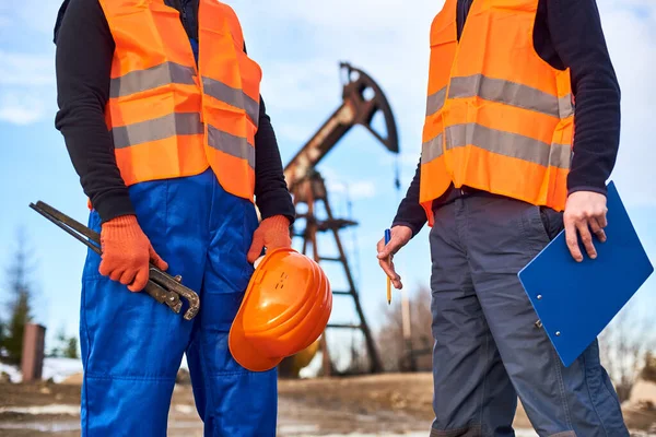 Großaufnahme Eines Tankstellenbetreibers Mit Industrieschlüssel Helm Neben Kollege Mit Klemmbrett Stockfoto