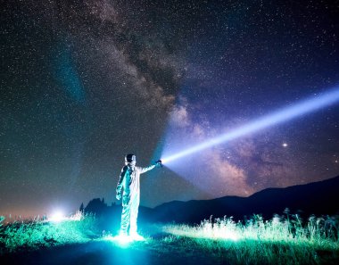 Astronotlar gökyüzünü el feneriyle aydınlatıyorlar. Kozmonot, parlayan çimlerin üzerinde dururken beyaz uzay giysisi ve kask giyiyor. Işık, galaksi ve astronotlar kavramı.